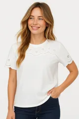 Remera blanca de algodón con cuello redondo y mangas cortas. Presenta bordado calado con motivos florales en el canesú y en los bordes de las mangas.