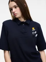Remera tipo polo blanca de manga corta con hombreras y pins removibles en la delantera.