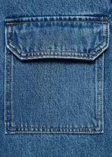 Campera de jean azul con corte recto, cuello camisero, cierre frontal con botones a presión, mangas largas con puños abotonados y dos bolsillos de parche con solapa en el pecho.