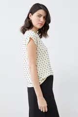 Blusa color crudo con estampado de puntos negros, de corte recto y manga corta.