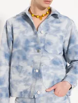 Chaqueta corta de algodón con estampado tie-dye en tonos celeste y blanco. Tiene cuello camisero, cierre con botones metálicos, bolsillos plaqué en el frente y remaches con brillos en el canesú de la espalda.