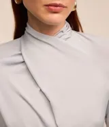 Blusa color gris claro con detalle drapeado en el cuello y mangas cortas.