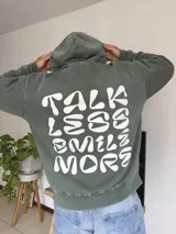 Canguro verde oliva con capucha y estampado en la espalda con la frase "Talk Less Smile More".