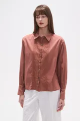 Camisa blanca de broderie con cuello camisero, cierre frontal de botones, mangas largas y corte holgado.