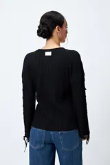Sweater negro de punto canalé con detalle de trenzado en las mangas y lazo ajustable en el ruedo.