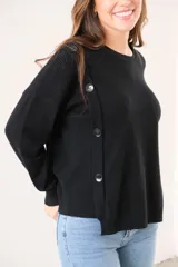 Sweater negro de punto con cuello redondo y corte recto. Presenta detalle de botones grandes en el hombro.