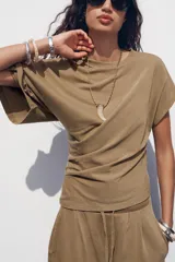 Camiseta color marrón con cuello redondo, manga sisa caída en un lado y manga corta en el otro. Tiene detalle de frunces laterales.