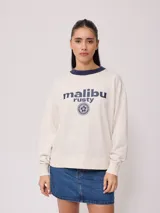 Sweater color crudo con cuello redondo azul marino y estampado frontal con el texto 'malibu rusty' y un logo con una flor.