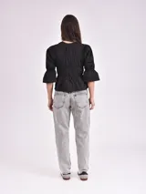 Blusa negra con escote mao y mangas 3/4 con volantes. Presenta detalle de frunces en el frente y lazos para ajustar.