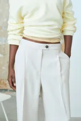 Pantalón sastrero color beige de sarga con pinzas, corte holgado, tiro alto, pretina prolongada con botón, bolsillos al bies y bolsillos insertados atrás. Piernas anchas con pliegues adelante y atrás.