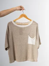Remera tejida color beige con cuello redondo y bolsillo frontal blanco.