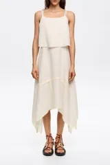 Vestido midi de algodón y lino color crudo, corte línea A con vuelo y bajo irregular. Presenta escote recto con tirantes finos y top superpuesto con bordados a contraste.