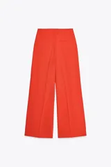 Pantalón de vestir color naranja, de tiro alto y pernera ancha. Presenta doble pliegue frontal, trabillas en la cintura, bolsillos laterales y falsos bolsillos de vivo en la espalda.