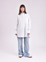 Camisa blanca de corte amplio, con cuello clásico, mangas 3/4 con puños arremangados y bolsillo de parche en el pecho.