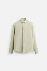 Camisa color arena de lino con cuello abotonado, manga larga con puños abotonados, corte regular y bajo con aberturas laterales.