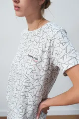 Conjunto de pijama blanco con estampado de corazones negros, compuesto por una remera de manga corta con bolsillo en el pecho y un pantalón largo de corte recto.