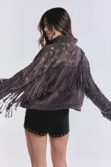 Campera marrón de gamuza sintética con flecos en el pecho y mangas, bordado de flores en el frente y cierre frontal con cremallera.