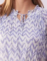Blusa de microtul estampada con diseño zigzag en tonos celeste y blanco, de la marca Cable & Gauge. Tiene cuello a la base con escote en V y lazo de ajuste, mangas cortas con puño elastizado y forro interno a tono.
