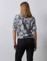 Blusa de gasa estampada color celeste con estampado paisley, marca Ruby Rd. Cuello a la base, escote en v y abertura con botones. Delantera con bolsillos. Largo de manga regulable con presilla y botón. Terminación de ruedo con nudo.