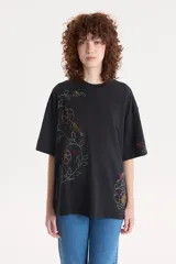 Remera negra de corte holgado con estampado floral en el lateral izquierdo y en la manga derecha.