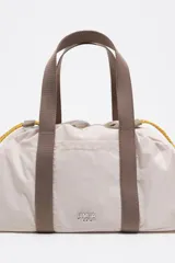 Mini bolso de nylon color marrón con asas de mano naranjas y cordones ajustables verdes. Incluye logo metálico de Bimba y Lola y bolsillo interior.