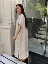 Vestido largo de tejido a rayas horizontales en tonos beige y blanco, con escote en V y mangas cortas tipo murciélago. Presenta tajos laterales en el ruedo.