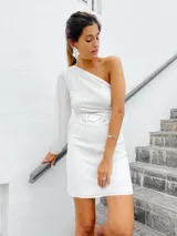 Vestido corto blanco con un hombro descubierto y una manga larga abullonada. Incluye cinturón con hebilla de alpaca y nácar.