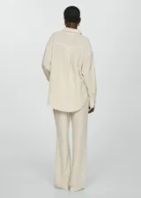 Camisa color crema de bambula con cuello camisero, diseño oversize, manga larga con puños abotonados, bolsillo de parche en la parte delantera y cierre delantero con botones.