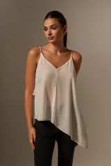 Blusa blanca de poliéster con breteles finos, escote en V, corte asimétrico y volados.