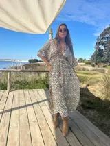Vestido largo de seda color crema con estampado geométrico en tonos camel y negro. Tiene escote en V, mangas cortas amplias y cintura ajustable con cordón.