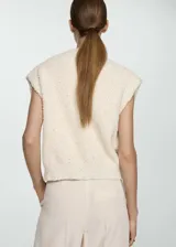 Chaleco de tweed color crema con lentejuelas, cuello redondo, cierre frontal con botones dorados y dos bolsillos de parche con botón.