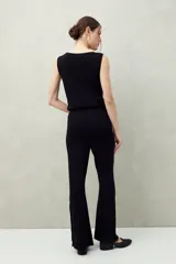 Pantalón negro de punto con calce relajado, caída fluida y botones dorados en los laterales.