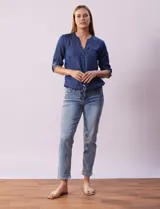 Blusa de tencel azul con cuello a la base y escote en V, abertura central con botones, bolsillos delanteros, mangas 3/4 regulables con presilla y botón, y terminación de ruedo con nudo.