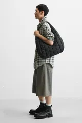 Bolso de hombro negro fabricado en tejido técnico acolchado con diseño geométrico. Tiene un compartimento principal con cierre mediante imán, un bolsillo plano y un bolsillo con cierre mediante cremallera en el interior.