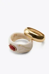 Pack de dos pulseras rígidas, una dorada de metal y otra de resina color crema con veta marrón y aplique de piedra ovalada color coral con engarce dorado.