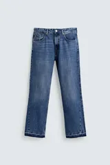 Pantalón de jean azul de corte flare, con tiro medio, cinco bolsillos y terminación desflecada en el ruedo. Cierre frontal con cremallera y botón.