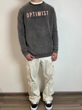 Buzo gris con efecto lavado y estampado con la palabra "OPTIMIST" en color salmón.