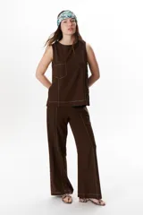 Top sin mangas color terracota con cuello redondo y bolsillo frontal. Presenta costuras a contratono en blanco que definen los bordes y el bolsillo.