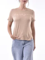 Remera blanca de algodón con cuello redondo y estampado frontal con la frase 'bloom with grace' en letras cursivas negras.