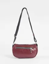 Riñonera cilíndrica de cuero vegano color borgoña, con dos compartimentos separados con cierres plateados. Posee una correa ajustable de tela negra y tiradores de cuero en las cremalleras.