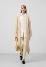Chaqueta larga color beige de punto doble frontura de galga fina, con solapa, manga larga, bolsillos delanteros y cinturón.