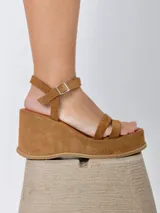 Sandalias de cuero color marrón con plataforma y taco de 8cm forrados en gamuza. Diseño con doble tira frontal y tira regulable al tobillo con hebilla metálica.