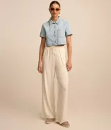 Camisa cropped de jeans celeste con cuello clásico, mangas cortas, cierre frontal con botones y bolsillo en el pecho.
