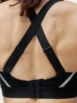 Top deportivo negro de alta sujeción con tirantes regulables cruzados y cierre ajustable en la espalda. Tejido Shape_Tech con tecnología performance y cinta reflectante.