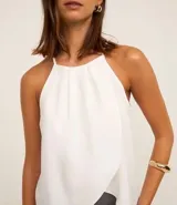 Blusa blanca sin mangas, con cuello halter y diseño cruzado en el frente.