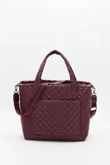 Bolso tote grande acolchado color vino tinto, con costuras en patrón de rombos. Posee dos asas de mano y una correa ajustable y desmontable con texto repetido. Incluye un charm colgante con letras negras.