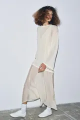 Vestido largo de punto ligero color crudo, con cuello redondo y mangas largas. Presenta un forro interior de tela satinada color beige claro que asoma en el bajo, creando un efecto de dos piezas.