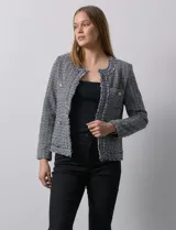 Chaqueta Nanette de tejido tweed color beige, con cuello a la base, abertura central y bolsillos delanteros. Tiene apliques de botones perlados en los puños, terminación desflecada y forro interno.