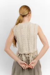 Chaleco de hilo color crema, con cuello redondo y diseño calado. Presenta flecos en el ruedo.