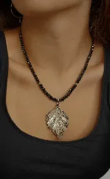 Collar de cristales facetados color negro, con dije de hoja plateada.